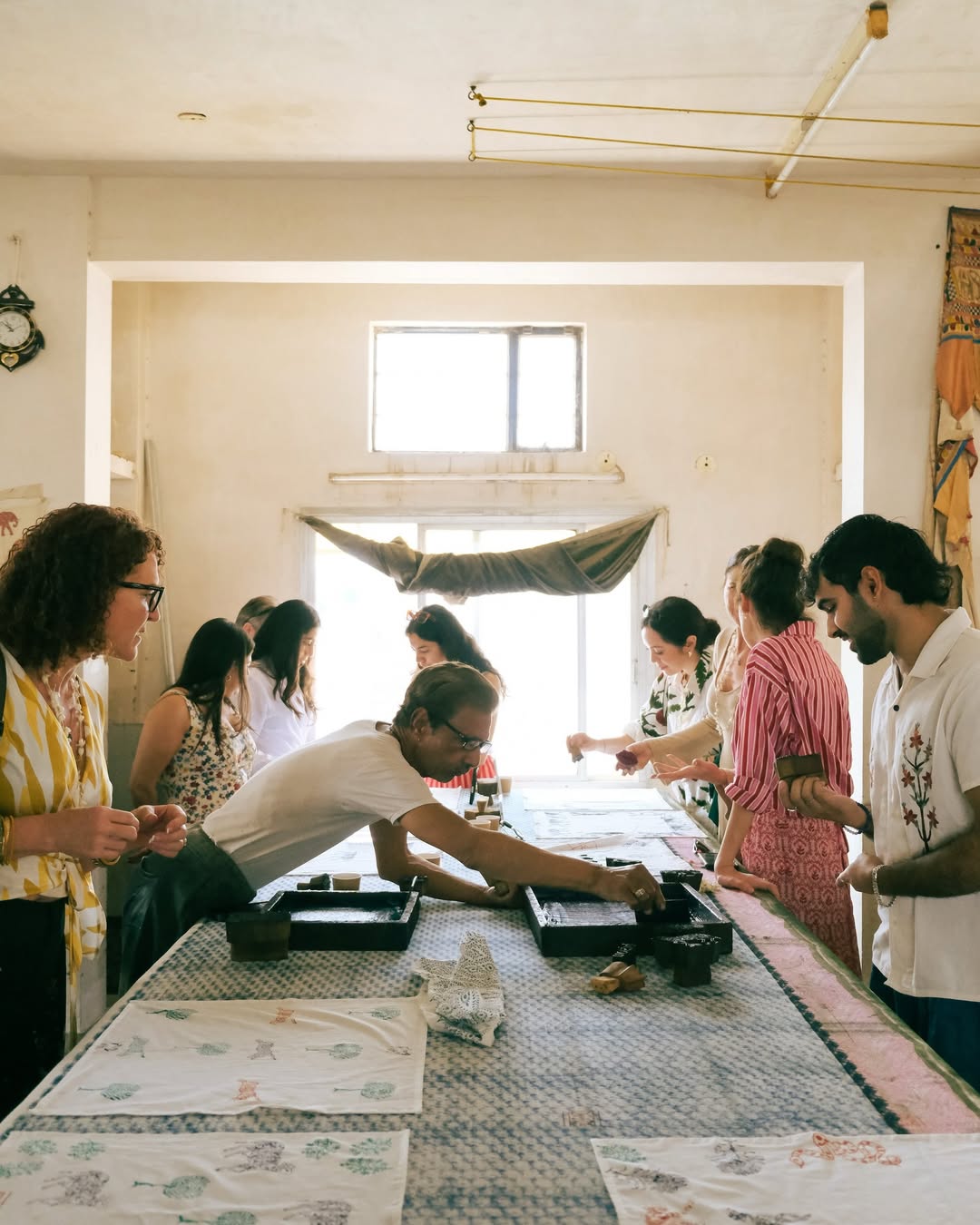 Group of people gathered around a table in a room with large windows for a block printing workshop.