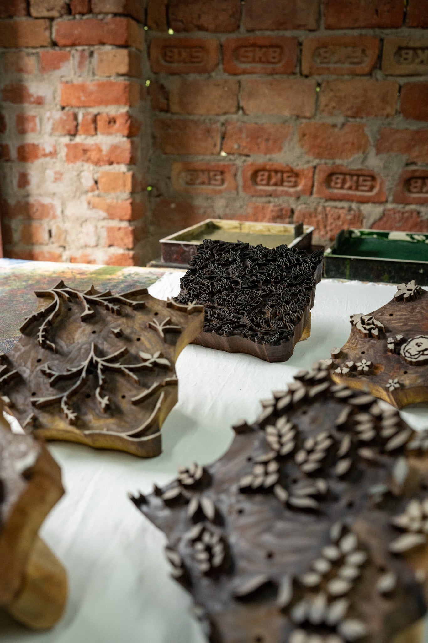 Wooden printing blocks with leaf patterns on a white surface against a brick wall background.