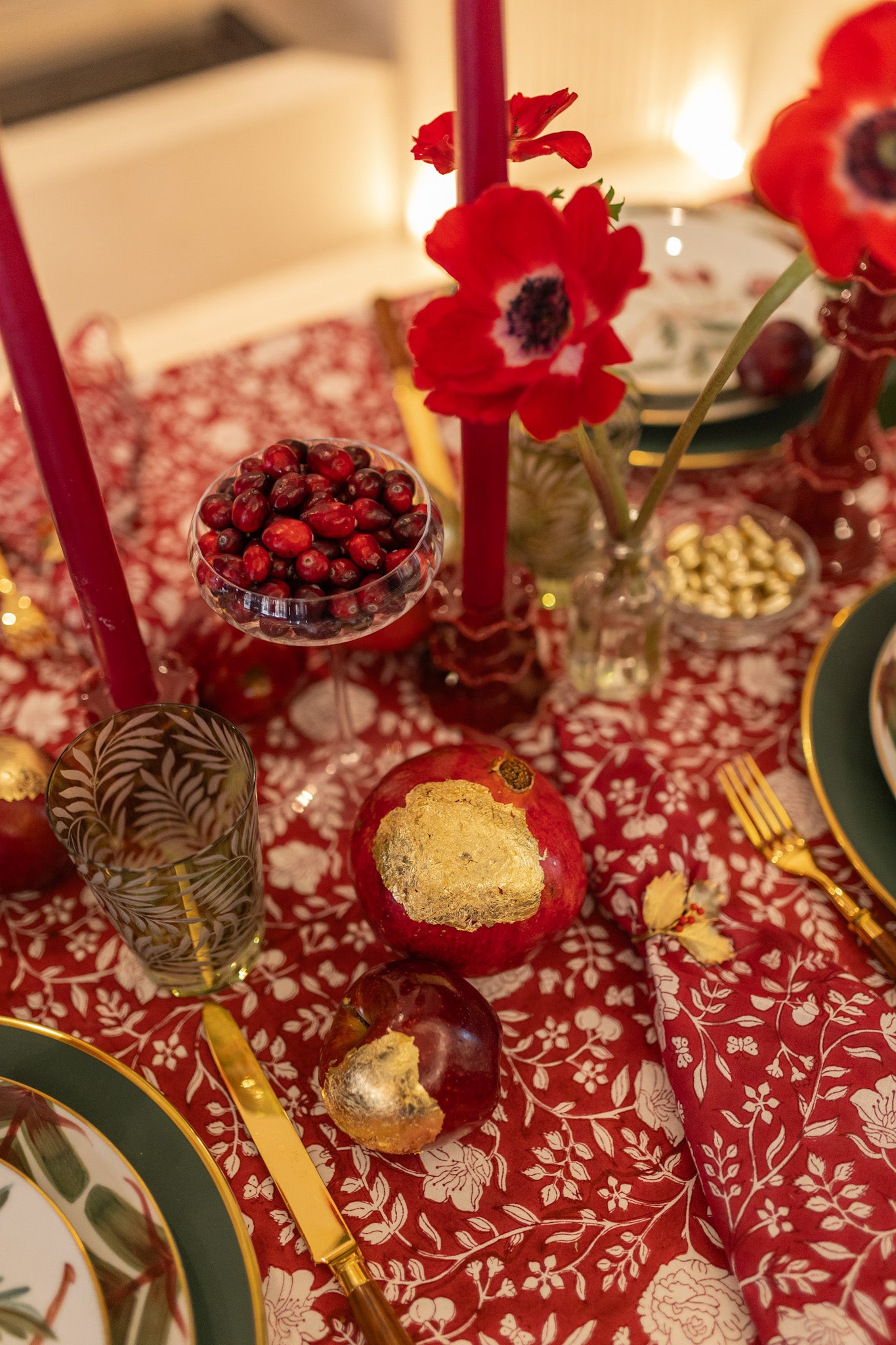 Decorative table setting with red candles, pomegranates, and gold accents on a patterned tablecloth.
