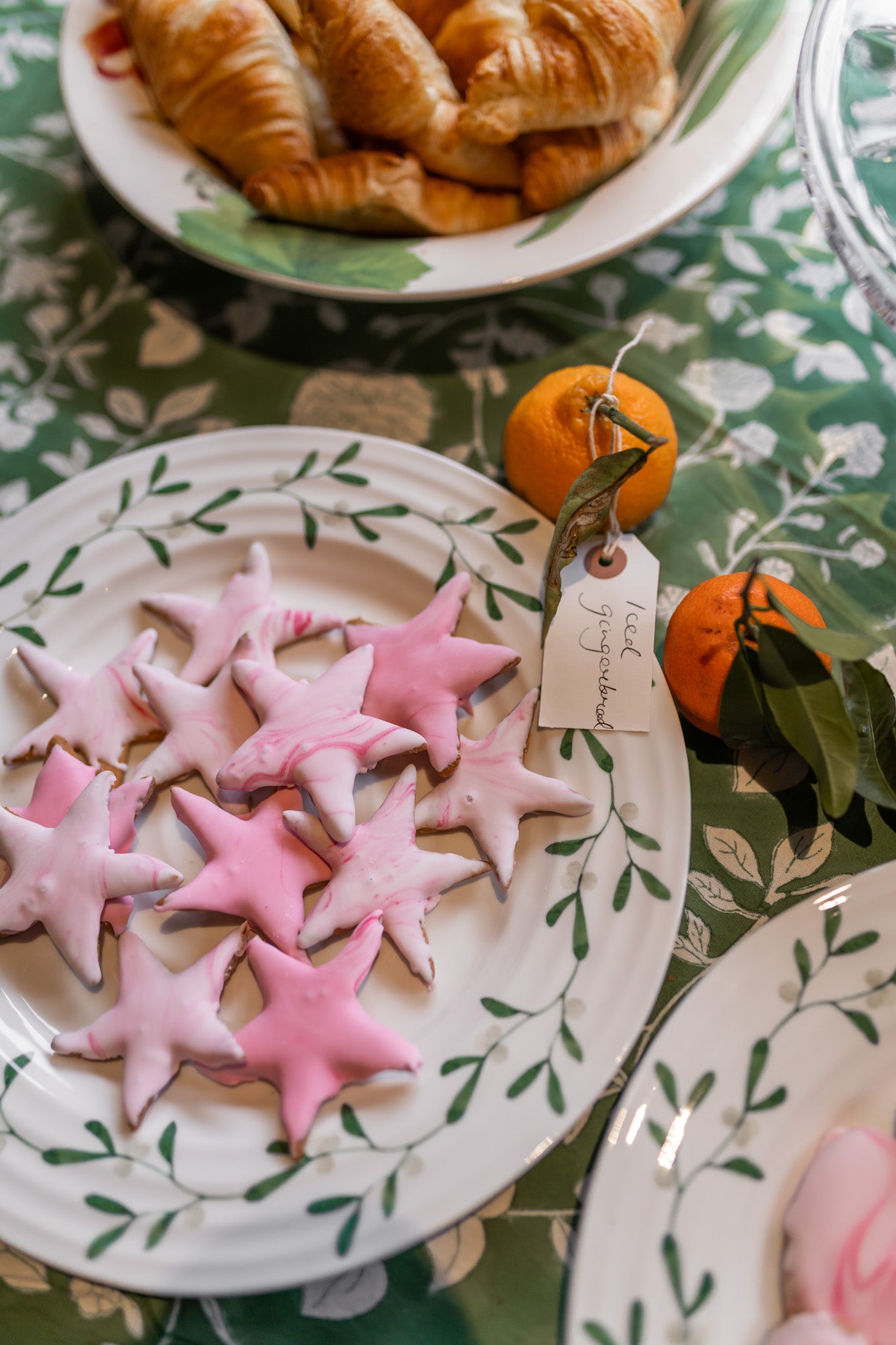 Star-shaped cookies on a decorative plate with a tag, oranges, and pastries in the background.