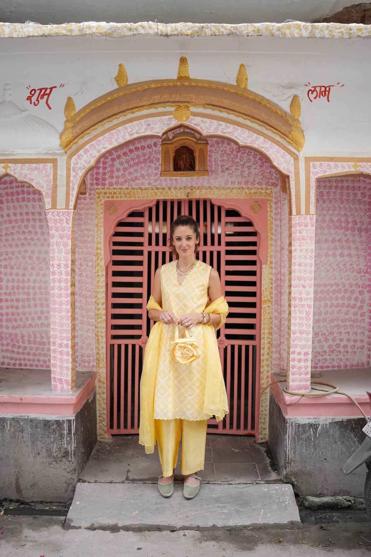 Pink door in Khajane Walon Ka Rasta Jaipur. Woman stands wearing yellow kurta outfit.