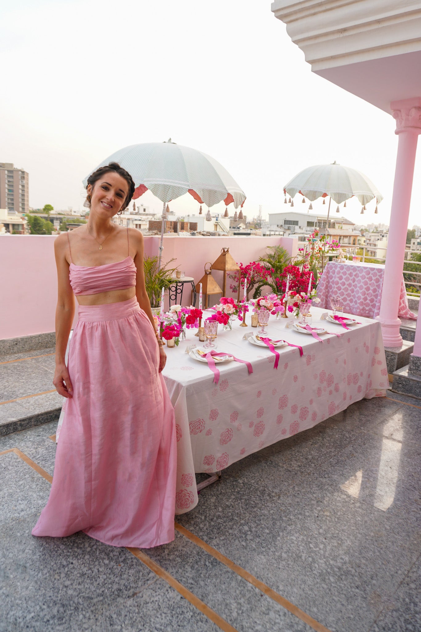 Pink tablescape in Jaipur with parasols in the background and Rosanna Falconer wearing pink skirt next to the table