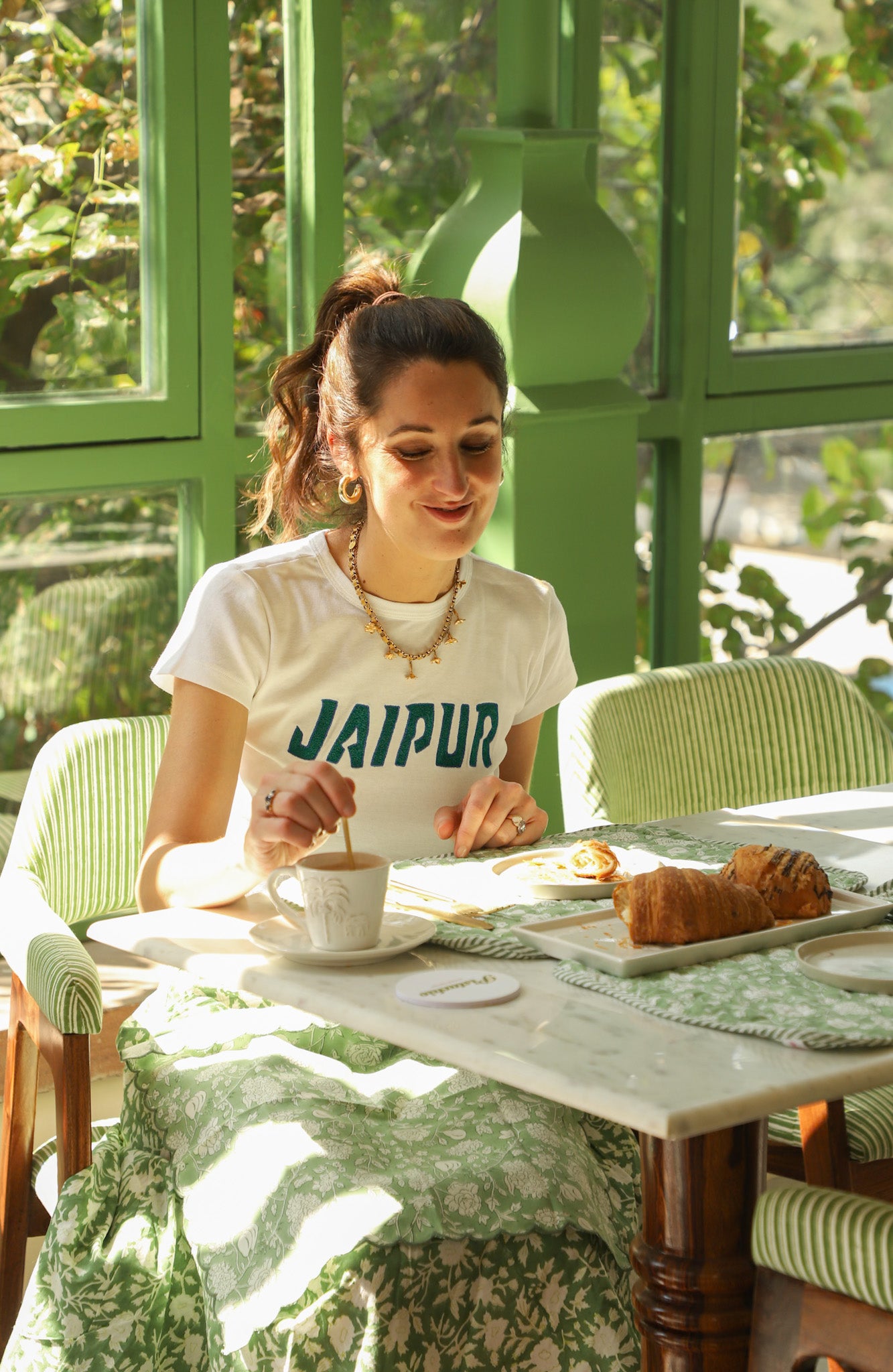 Woman sitting at a table with a cup of coffee, surrounded by greenery