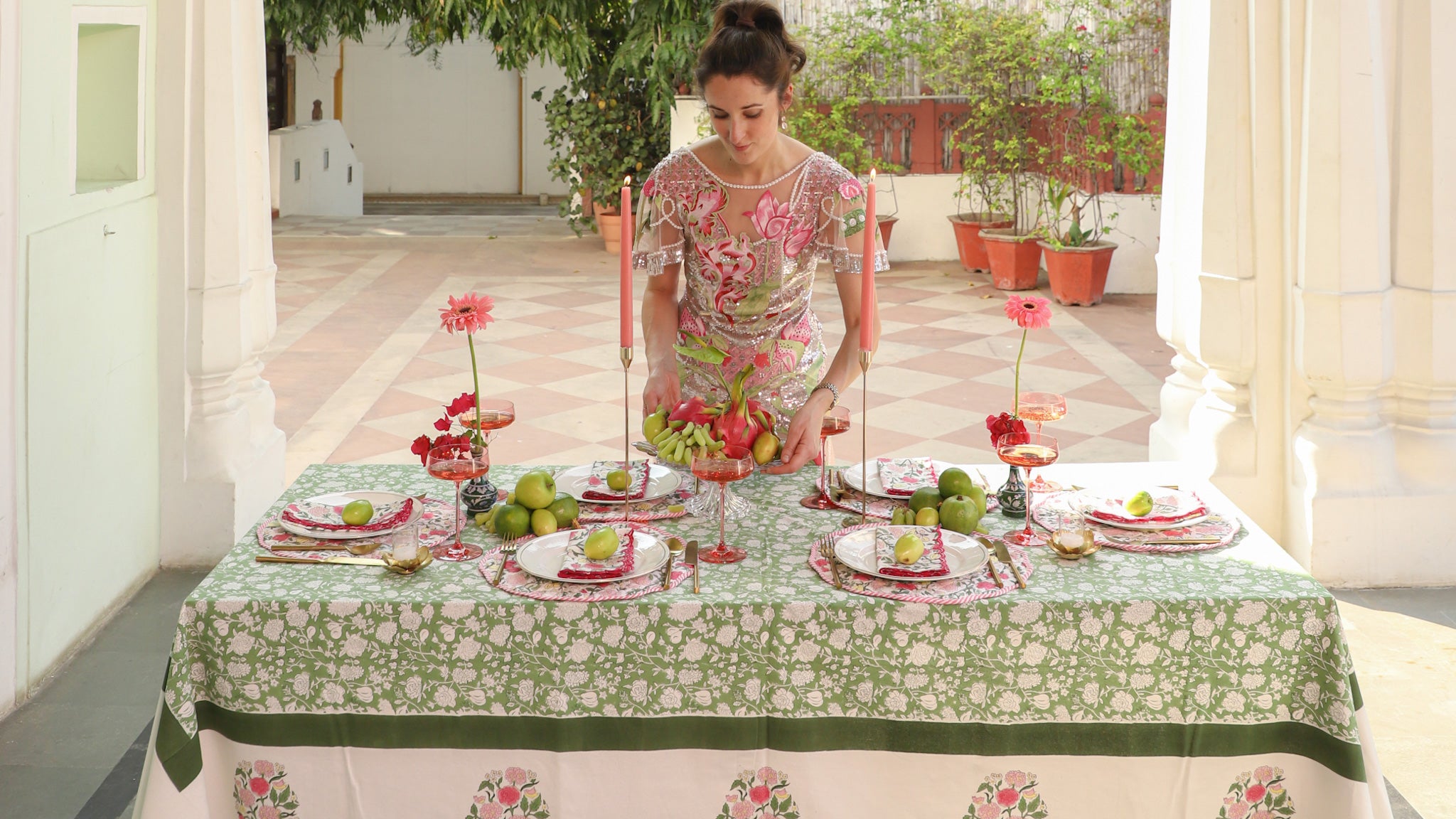 Woman arranging table settings with floral and green tablecloth in an outdoor setting.