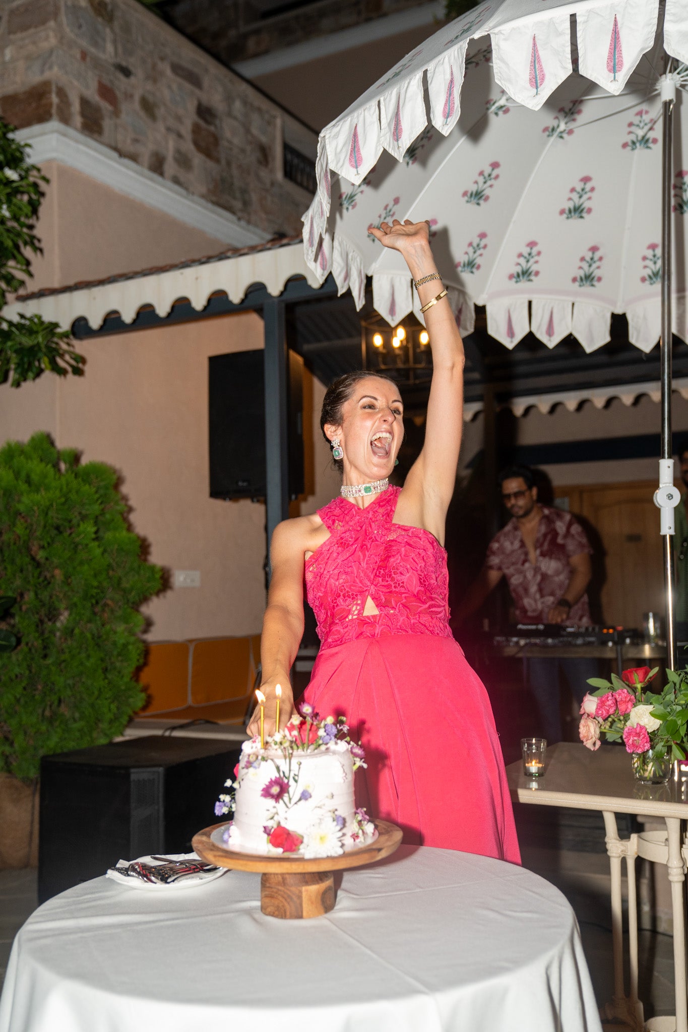 Woman in a pink dress celebrating with a cake under an outdoor canopy.