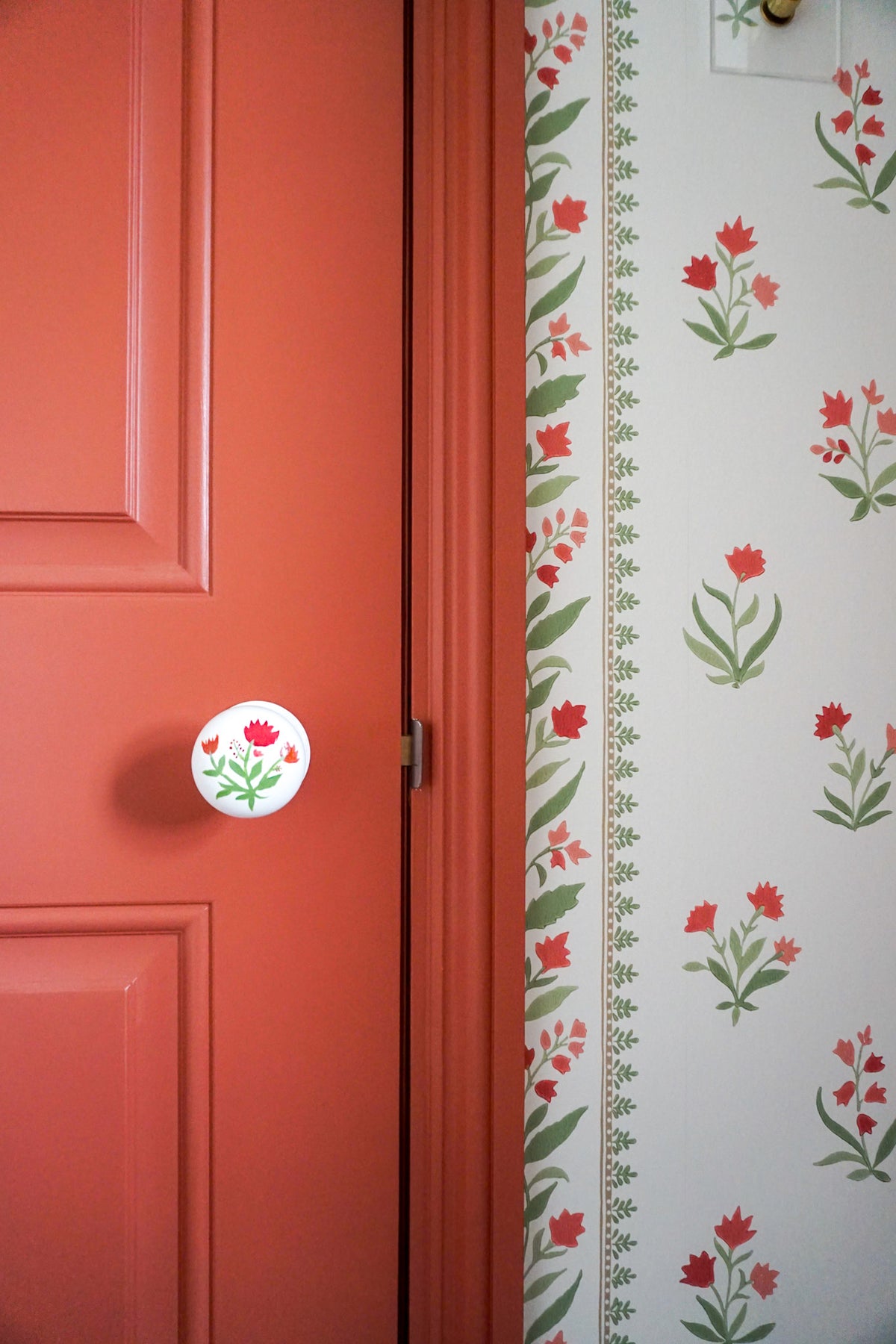 Red door with hand painted floral door knob. The wallpaper is block printed floral stripe with red and green.