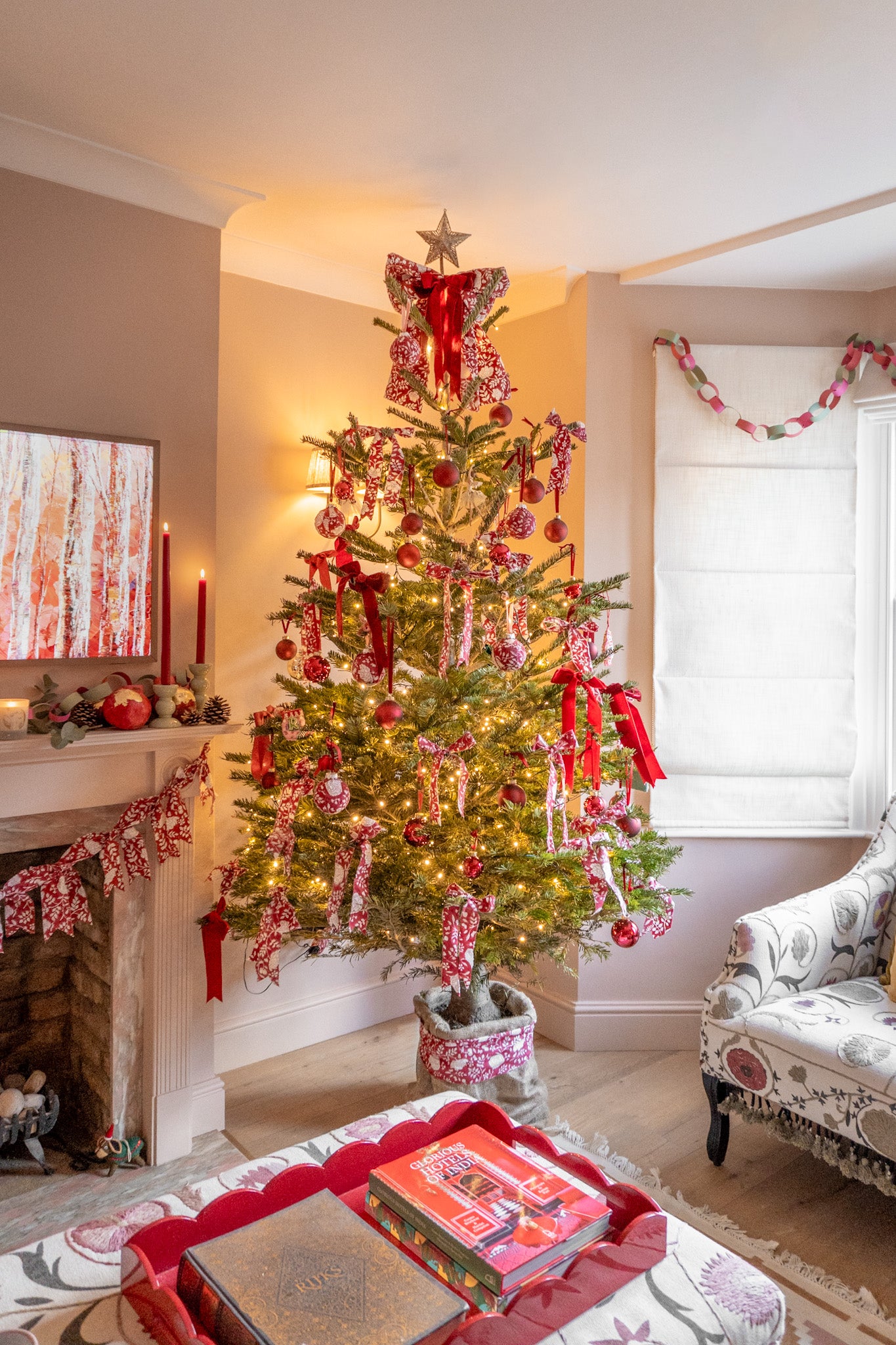 Decorated Christmas tree in a living room with a fireplace and books on a table.